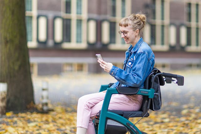 young woman in a wheelchair in the park reading something on a cell phone