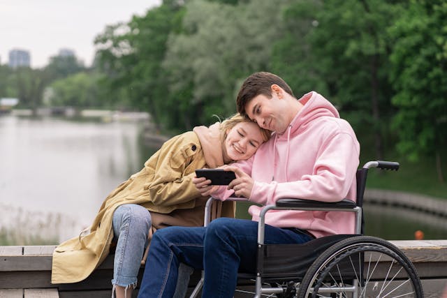 person in a wheelchair talking to a girl by the lake